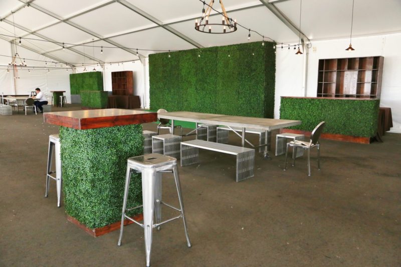 Greenery and event tables for an outdoor event in a tent.